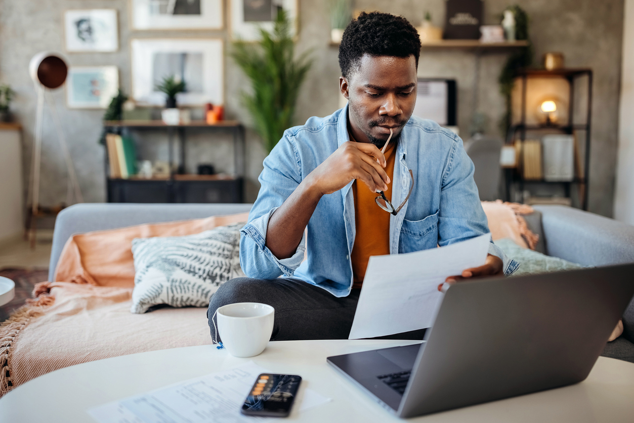 Man reviewing paperwork for insurance while sitting on couch in home.