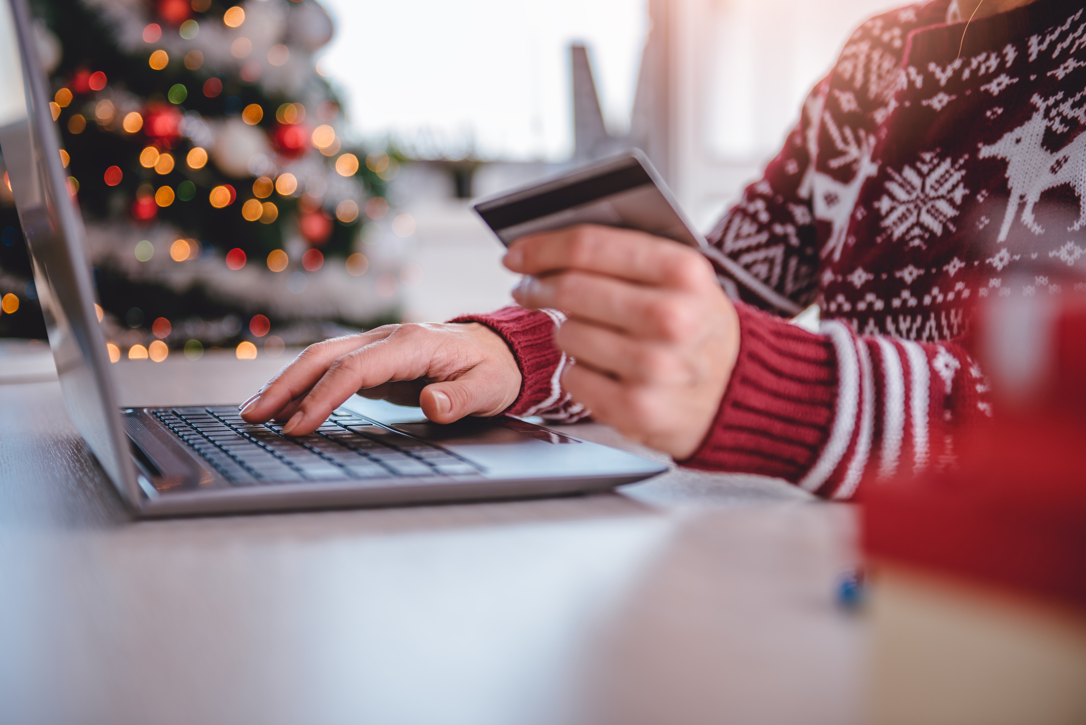 Close up shot of a person's hands working at a laptop with a credit card in their hand